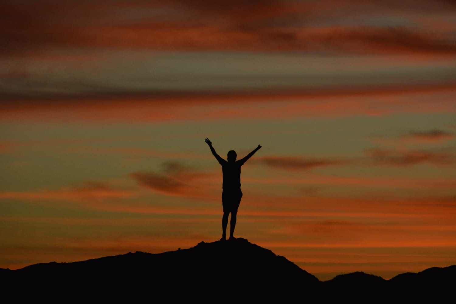 Silhouette d'un homme au coucher de soleil, bras levés